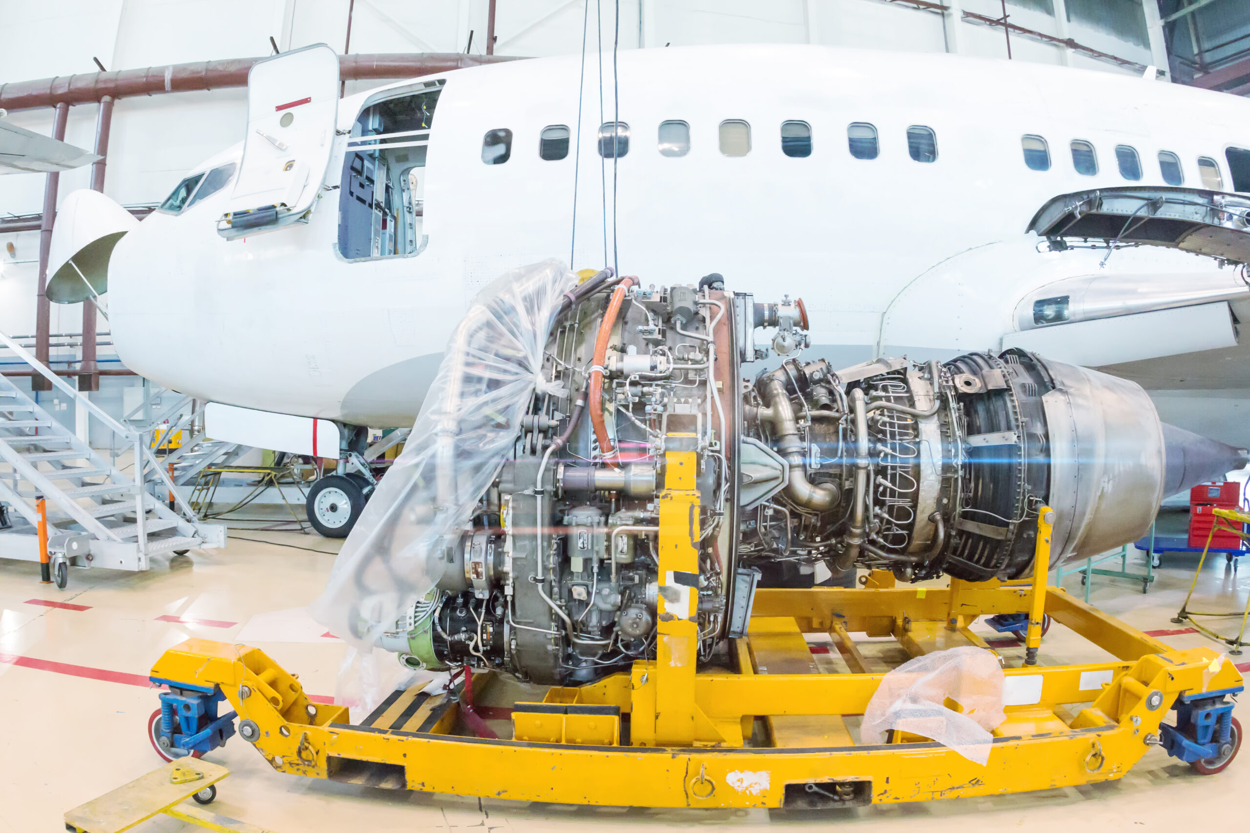 Close-up of high-bypass turbofan aircraft engine near to a passenger aircraft in a hangar